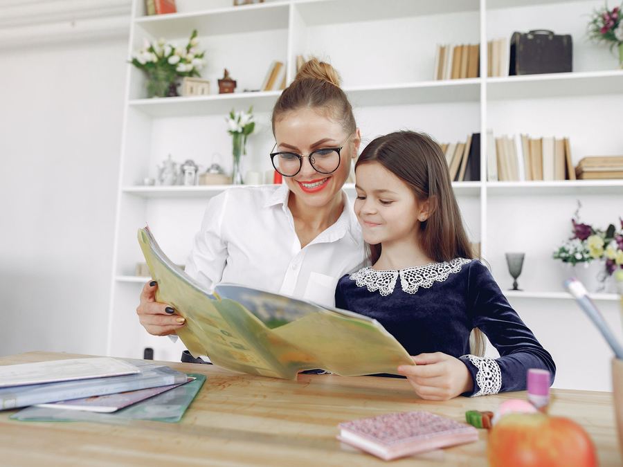 Maestra leyendo un libro con una alumna de uniforme
