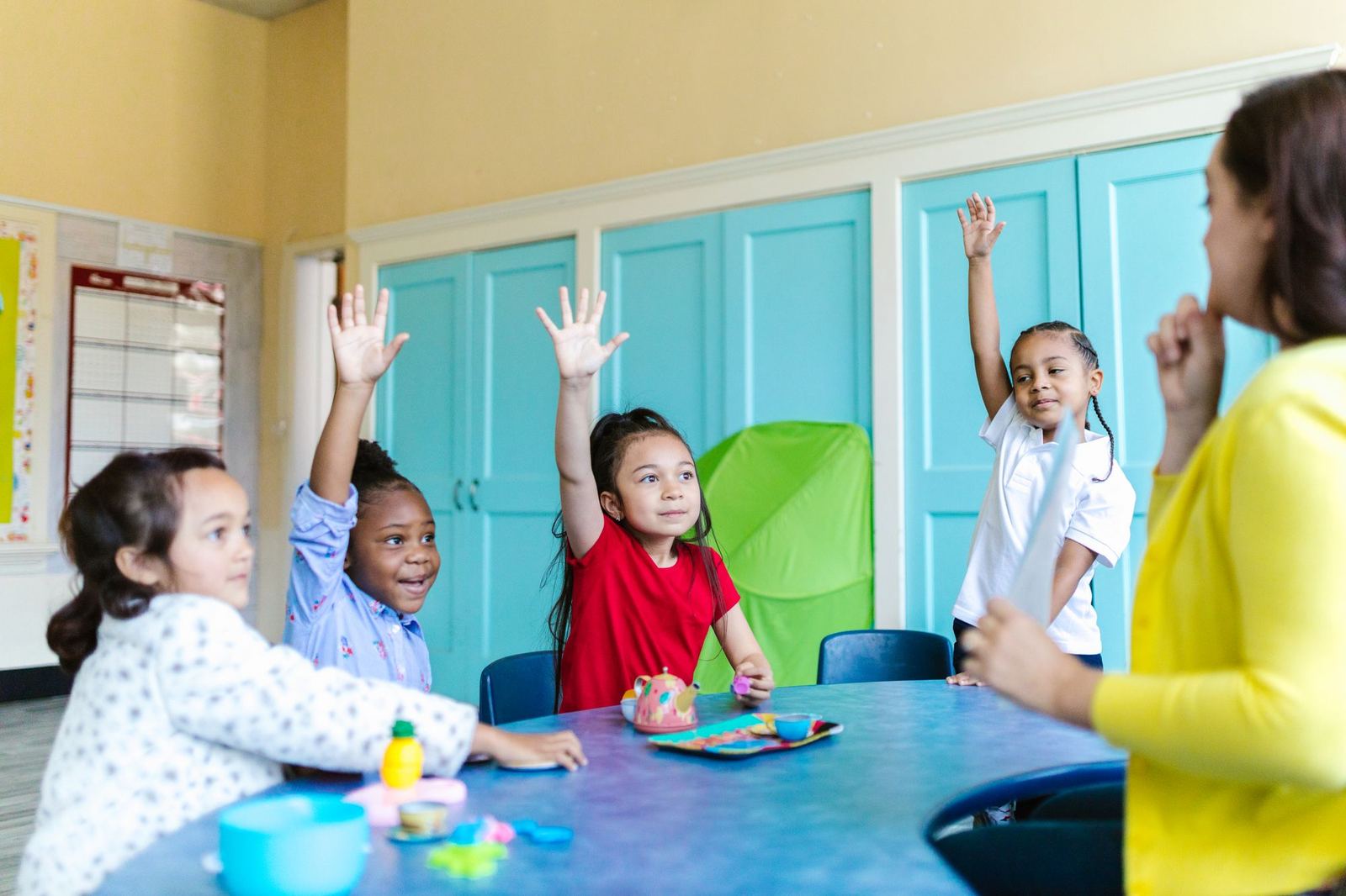 Maestra con alumnos de primaria levantando la mano en el salón